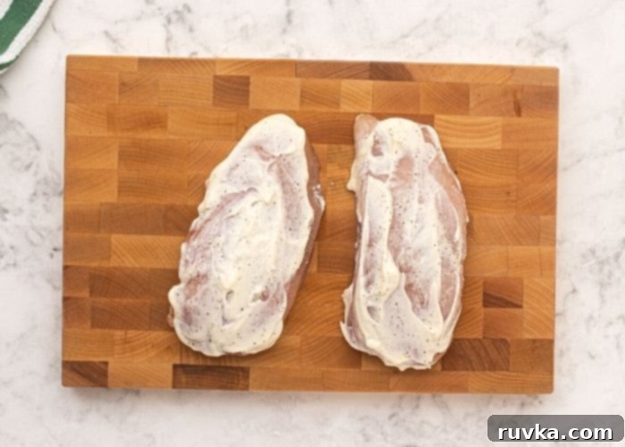 Crispy Pistachio Air Fryer Chicken 4 Uncooked chicken on a cutting board, seasoned with salt and pepper, then covered in mayonnaise.