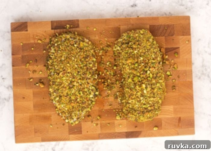 Crispy Pistachio Air Fryer Chicken 5 Uncooked chicken on a cutting board, seasoned with salt and pepper, then covered in mayonnaise and chopped pistachios.