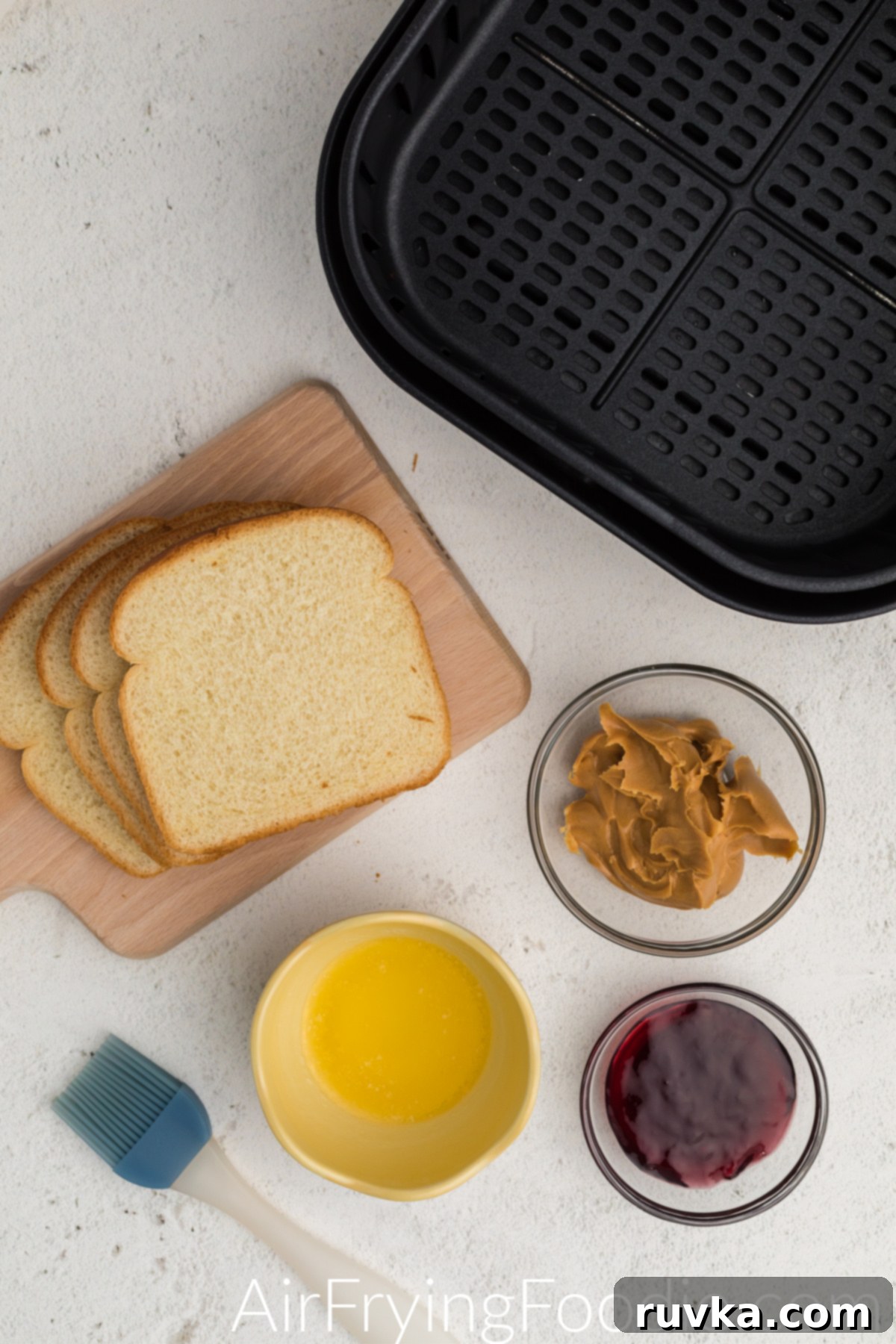 Crispy Air-Fried Peanut Butter and Jelly 3 Ingredients for making fried peanut butter and jelly in the air fryer, including bread, peanut butter, jelly, and melted butter.