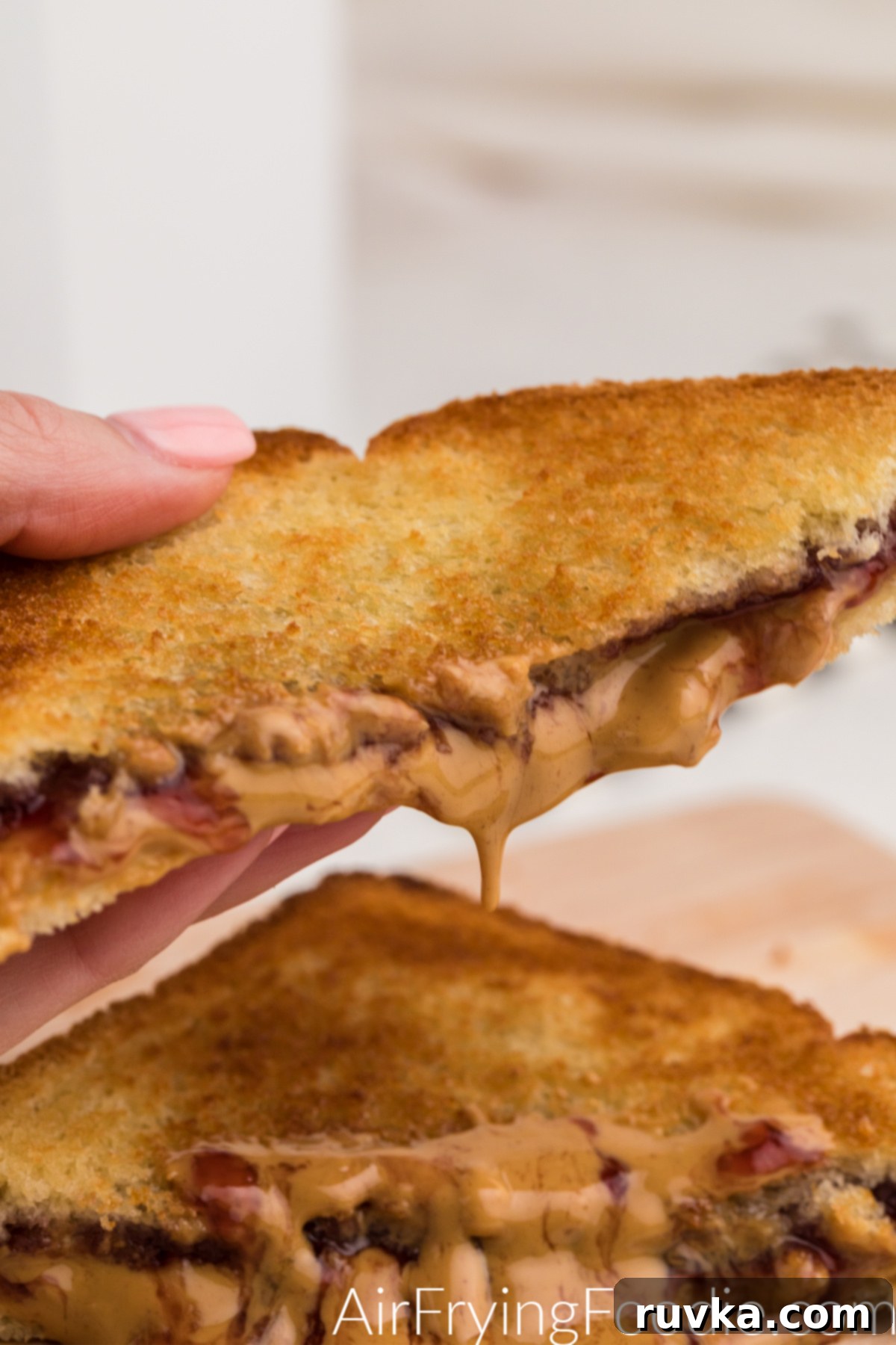 Crispy Air-Fried Peanut Butter and Jelly 8 Hand holding a slice of air fried peanut butter and jelly sandwich, showing the melted peanut butter and jelly oozing out.