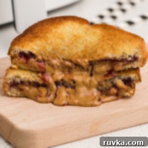 Crispy Air-Fried Peanut Butter and Jelly 9 Sliced air fried peanut butter and jelly sandwich, golden brown with melted fillings, on a cutting board.