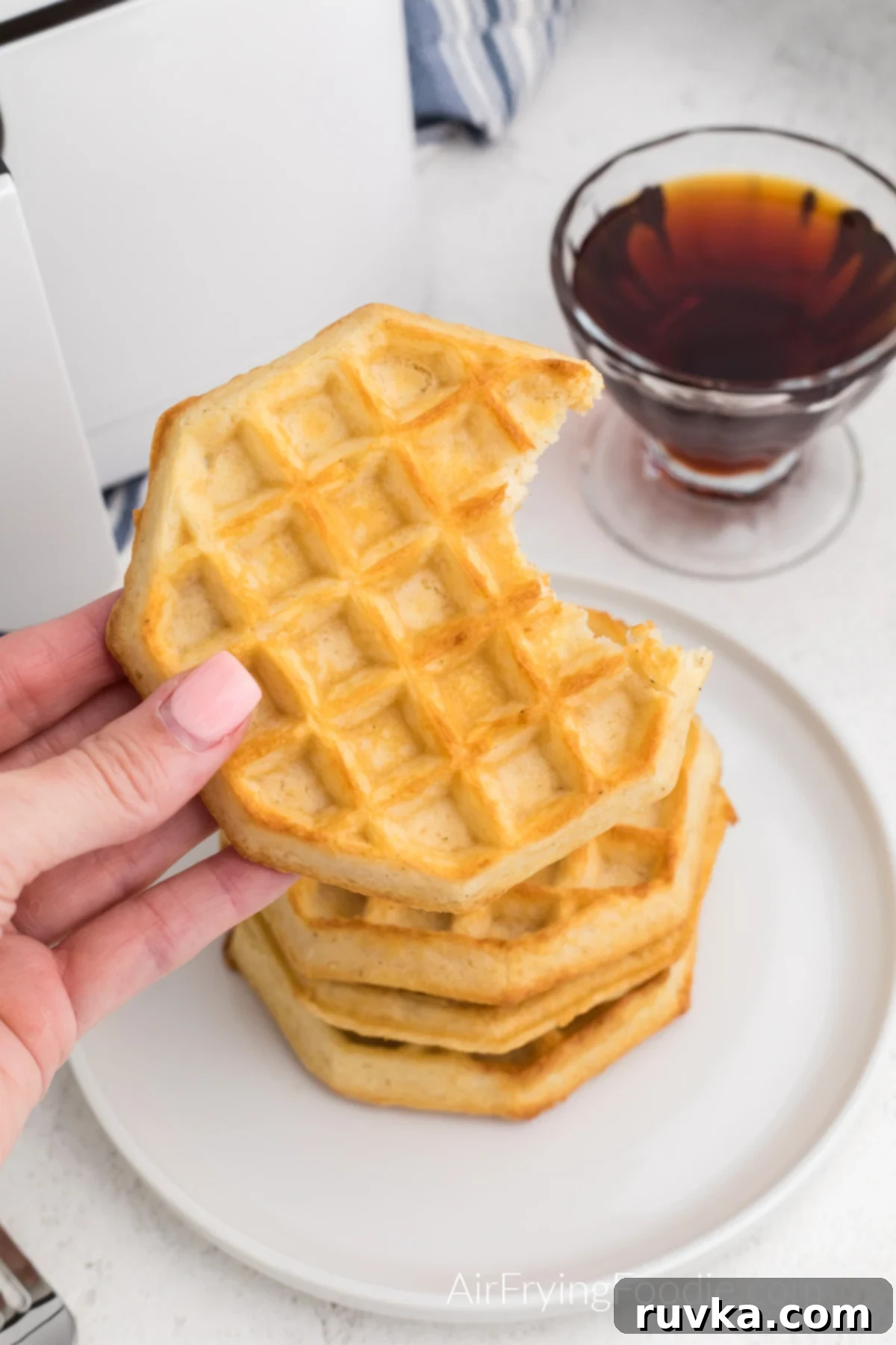 Frozen Waffles: Air Fryer Perfection 2 Waffles made in the air fryer from frozen, stacked on a plate, with a hand holding one that is missing a bite.