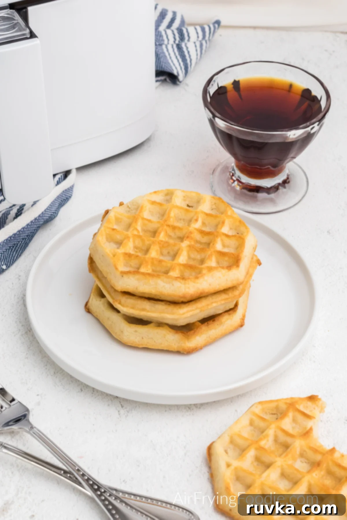 Frozen Waffles: Air Fryer Perfection 6 Air fried waffled made from frozen on a plate and one on the table that is missing a bite.