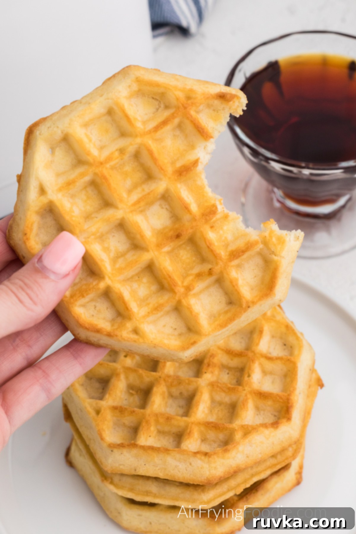 Frozen Waffles: Air Fryer Perfection 7 Close up of frozen waffles fully cooked in the air fryer, with a hand holding one that's missing a bite.