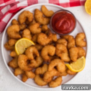 Crispy Frozen Popcorn Shrimp in Air Fryer 8 Overhead shot of golden brown frozen popcorn shrimp fully cooked in the air fryer and served on a white plate with dipping sauce and lemon wedges.