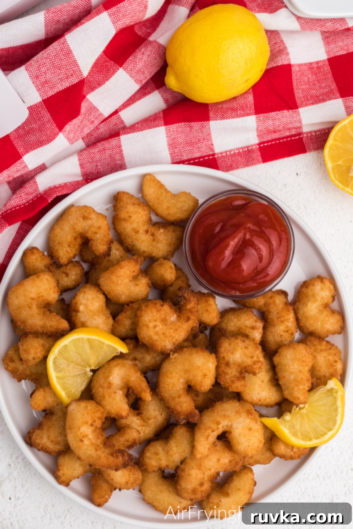 Crispy Frozen Popcorn Shrimp in Air Fryer 3 Overhead shot of popcorn shrimp made from frozen in the air fryer and served on a white plate with lemon wedges and dipping sauce.