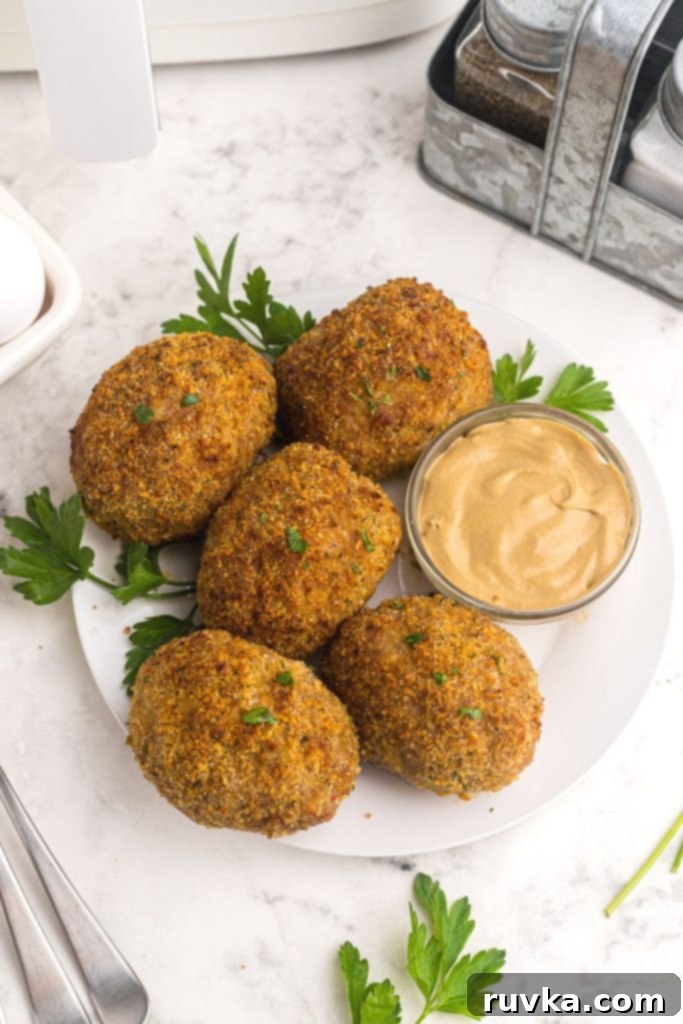 The Best Air Fryer Scotch Eggs 3 Crispy coated hard boiled eggs on a white plate garnished with parsley