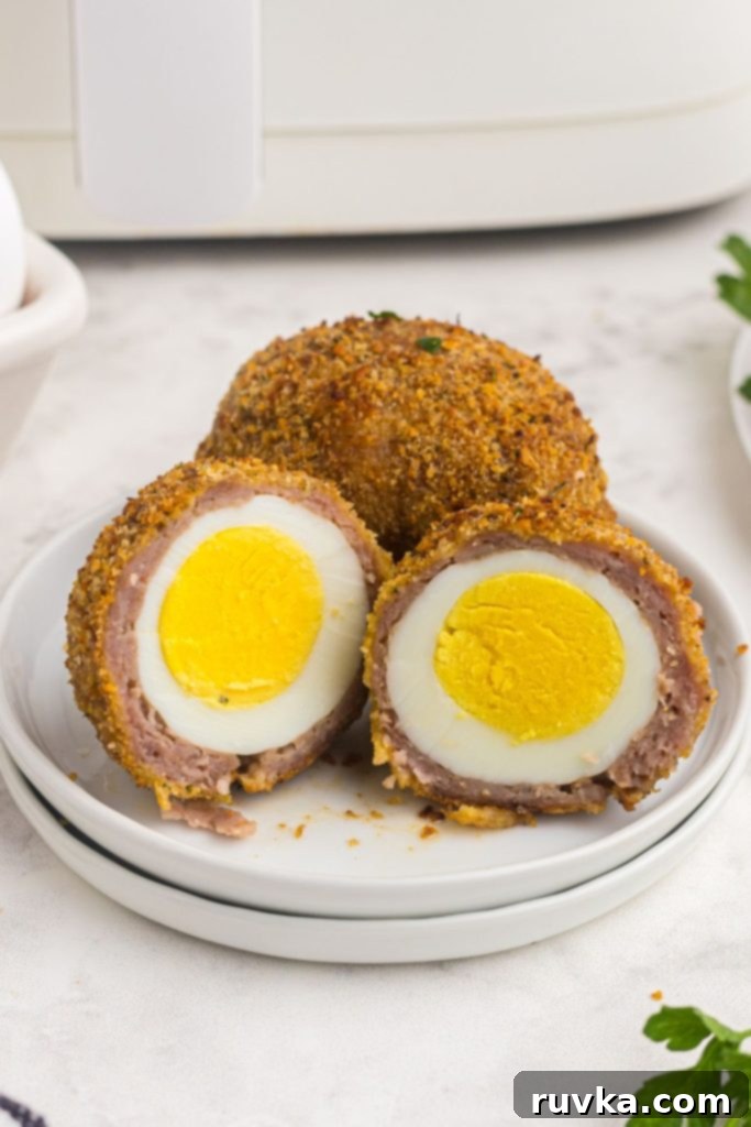 The Best Air Fryer Scotch Eggs 9 close up photo of scotch egg cut open showing hard boiled egg coated with pork sausage and crumbs
