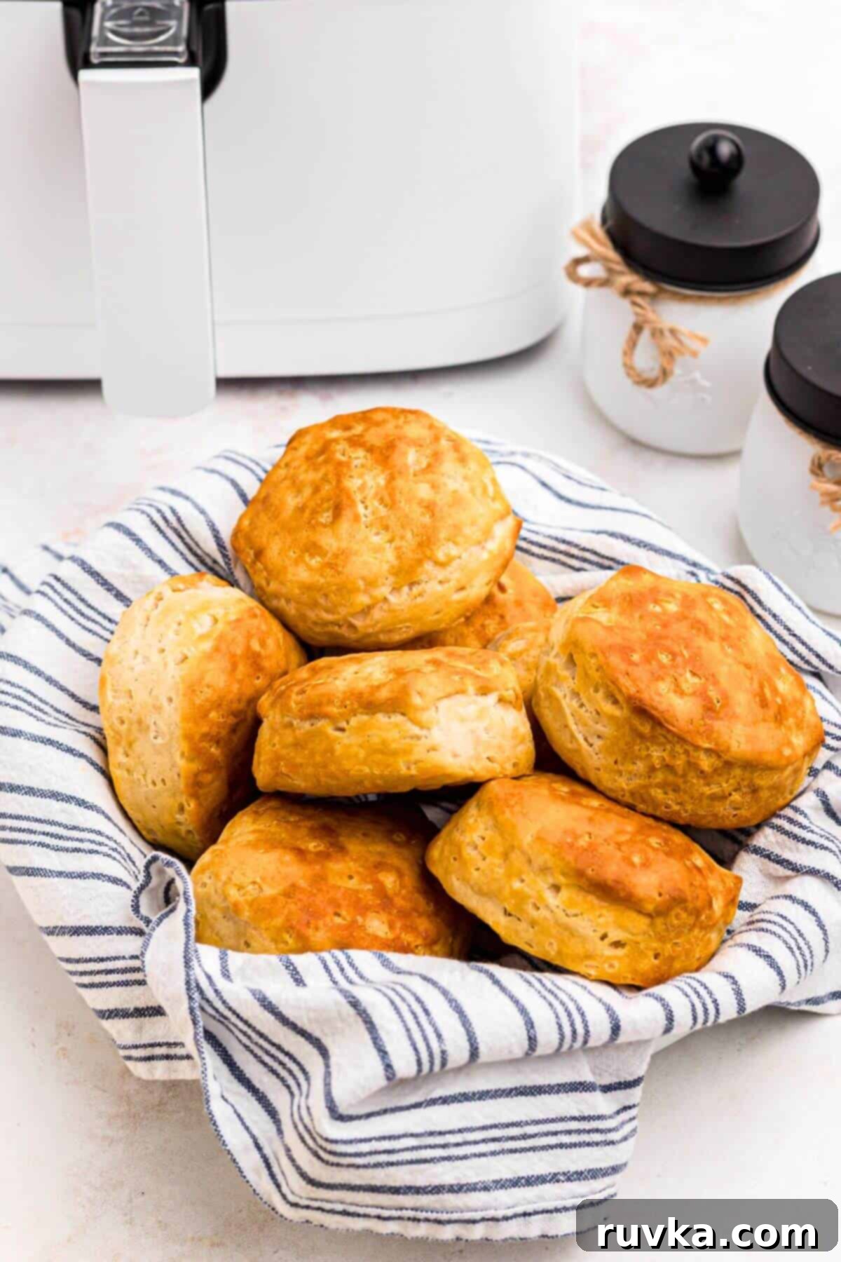 Fluffy Air Fryer Biscuits 6 Golden biscuits stacked in a basket in front of the air fryer.