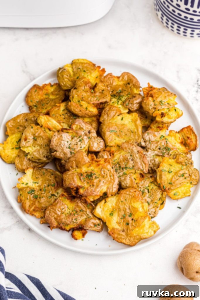 Air Fryer Crispy Smashed Potatoes 2 Golden crispy smashed potatoes on a white plate and seasoned, garnished with fresh herbs.