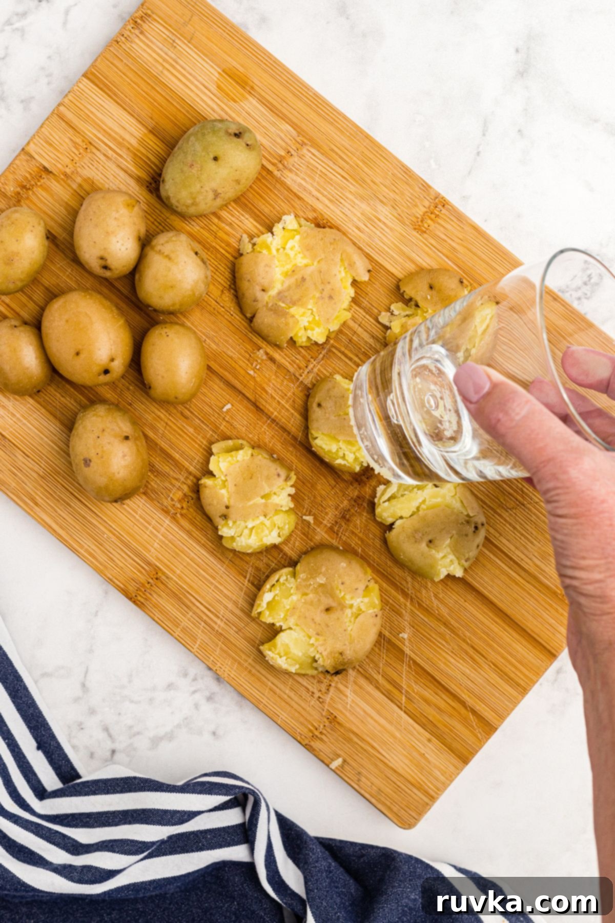 Air Fryer Crispy Smashed Potatoes 5 Soft golden potatoes on a wooden cutting board being smashed with a clear glass to create flat discs.