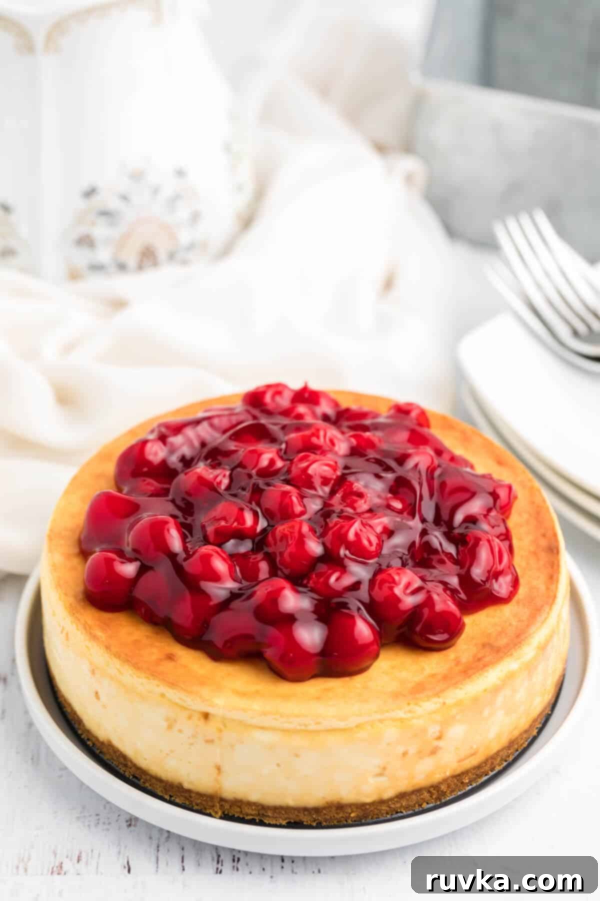 Perfect Air Fryer Cheesecake 2 A stunning cherry-covered air fryer cheesecake, perfectly sliced and served on a pristine white plate, showcasing its creamy texture and vibrant topping.
