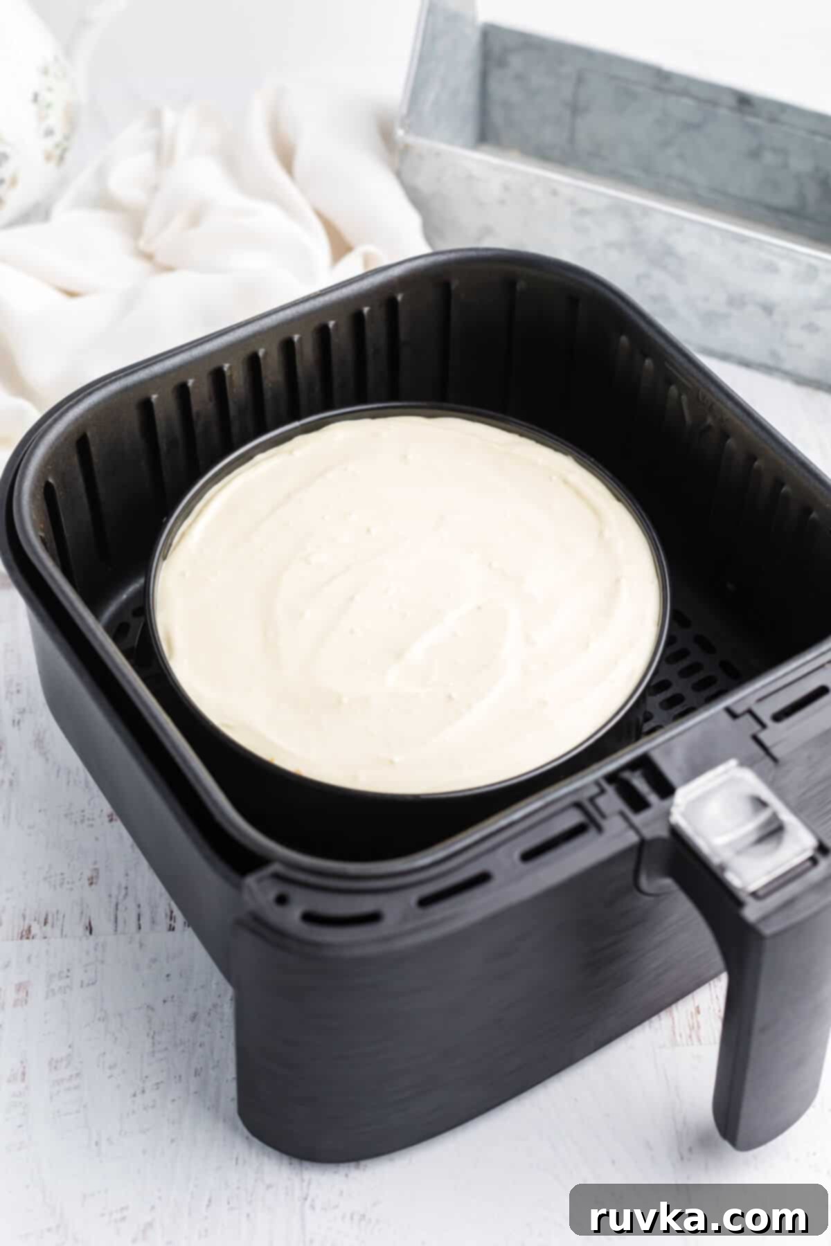 Perfect Air Fryer Cheesecake 5 The cheesecake filling has been poured over the graham cracker crust in a springform pan and is now placed inside the air fryer basket, ready for cooking.