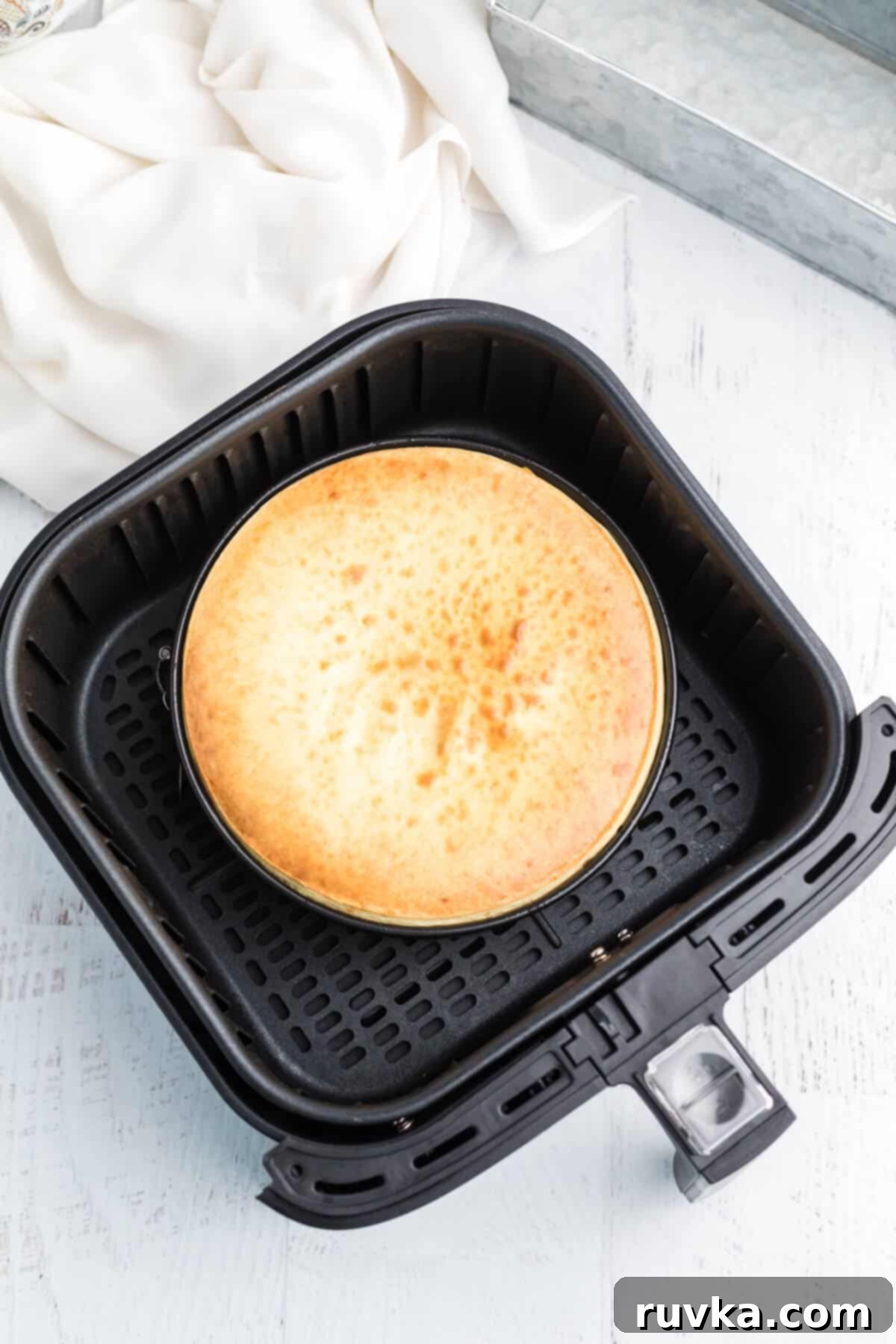 Perfect Air Fryer Cheesecake 6 A perfectly cooked air fryer cheesecake sits golden brown in the air fryer basket, cooled and ready to be removed for chilling.