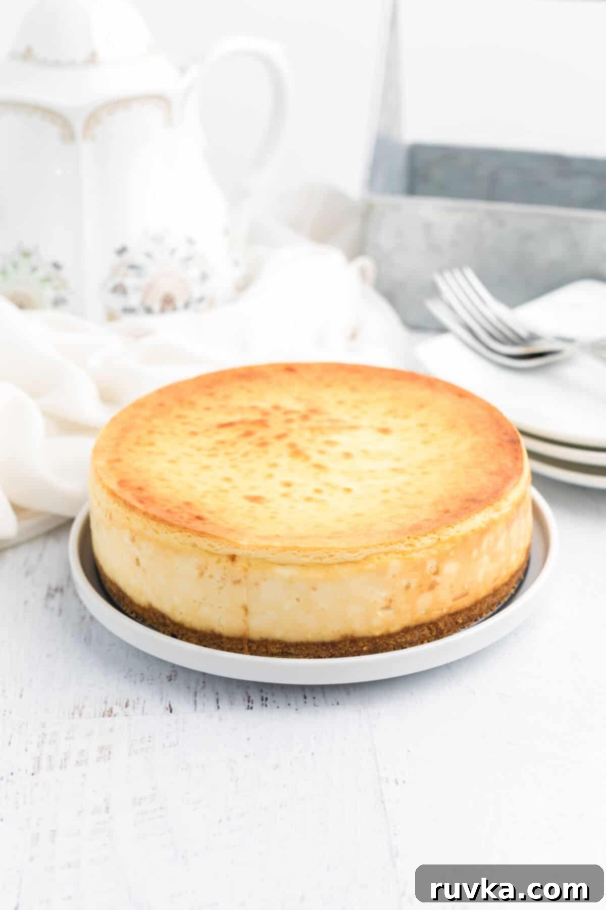 Perfect Air Fryer Cheesecake 7 A fully cooked and chilled air fryer cheesecake, beautifully removed from its springform pan, sits on a serving platter, awaiting its cherry topping and subsequent slicing.