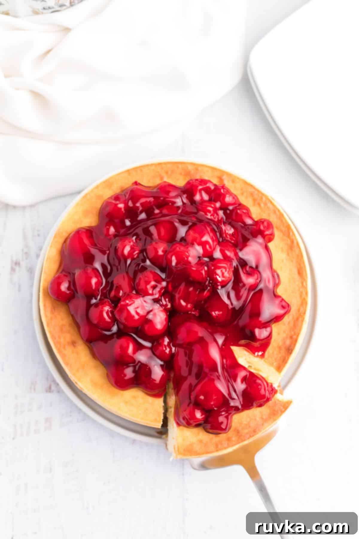 Perfect Air Fryer Cheesecake 9 A delectable air fryer cheesecake with a generous cherry topping is being expertly sliced and served, highlighting its irresistible appeal.