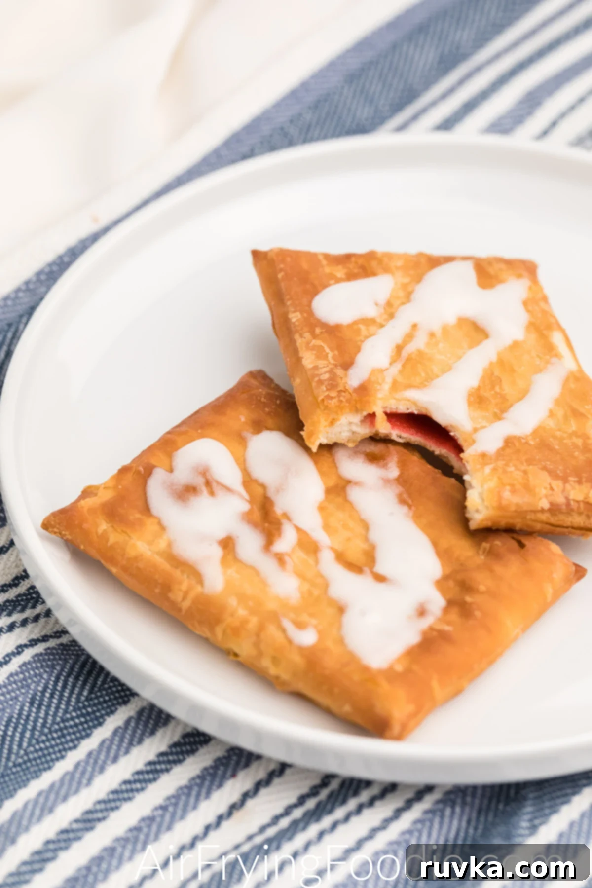 Flaky Air Fryer Strudel Bliss 2 Toaster Strudel made in the air fryer and topped with frosting, served on a white plate. One strudel is missing a bite.
