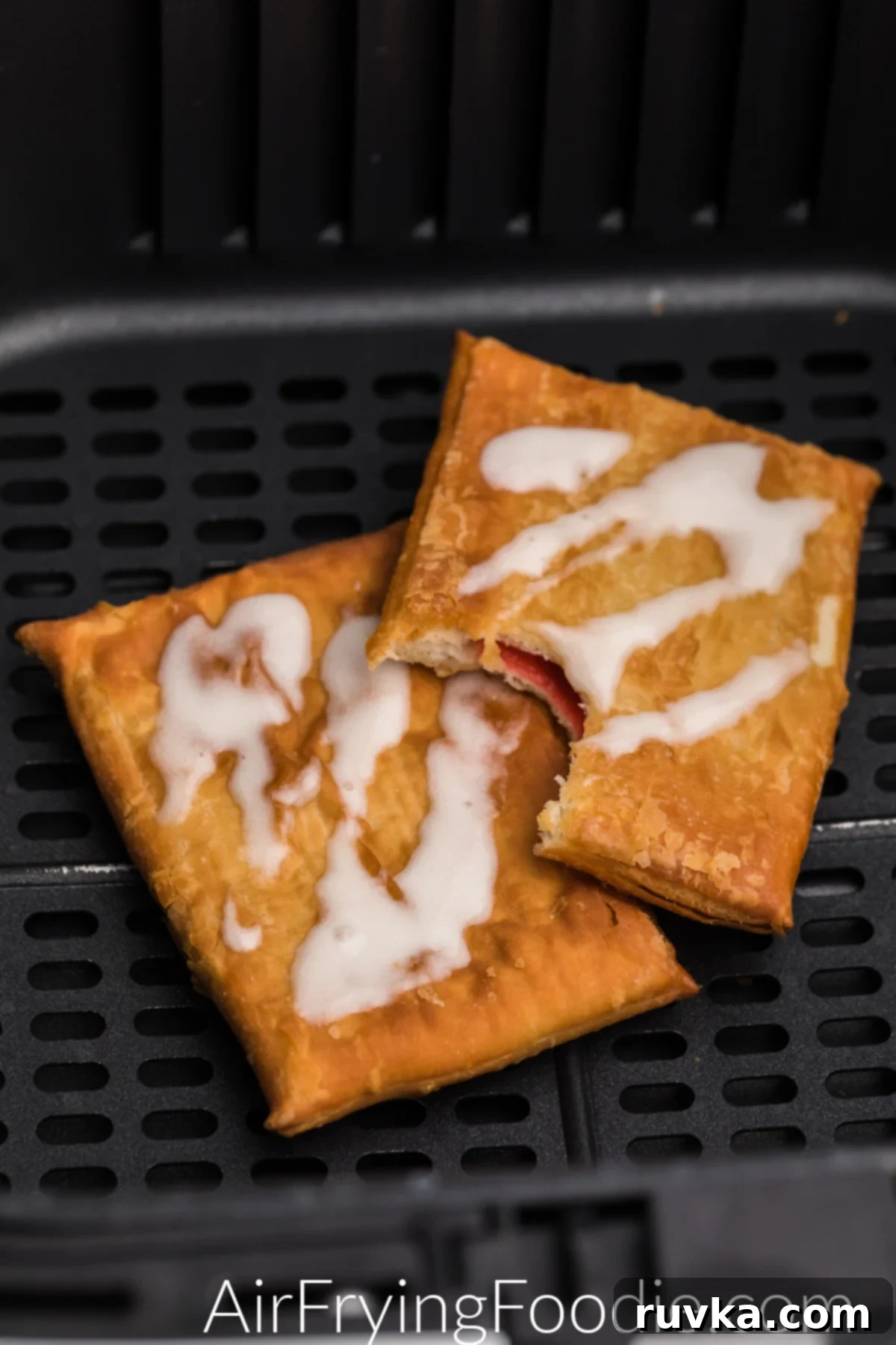 Flaky Air Fryer Strudel Bliss 3 Toaster strudel in air fryer basket with frosting, and one missing a bite.