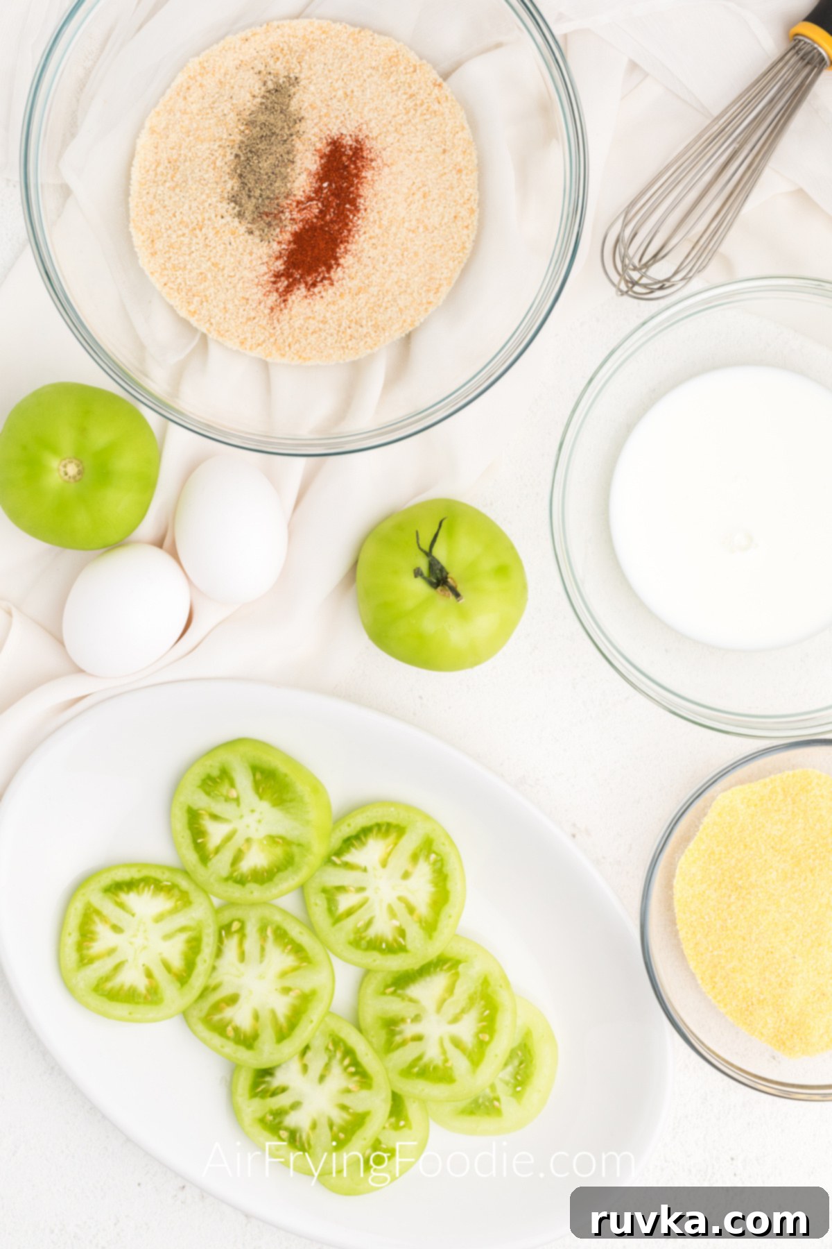 Crispy Air Fryer Fried Green Tomatoes 4 Sliced green tomatoes on a white plate with ingredients surrounding them on a table.
