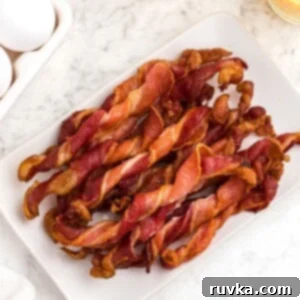 Easy Air Fryer Breakfasts 11 A stack of crispy, twisted bacon, freshly made in the air fryer, served on a white square plate alongside orange juice and eggs.
