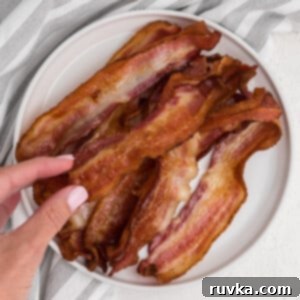 Easy Air Fryer Breakfasts 12 A hand reaching for a piece of perfectly crispy air fryer bacon on a white plate, highlighting its irresistible texture.