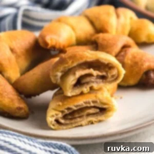 Easy Air Fryer Breakfasts 14 Golden, filled crescent rolls on a white plate, with one cut in half to reveal a sweet cinnamon mixture in the center.