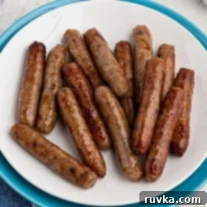 Easy Air Fryer Breakfasts 17 A white plate filled with crispy, golden brown sausage links, perfectly cooked in an air fryer, set on a marble table.