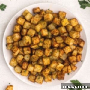 Easy Air Fryer Breakfasts 4 Crispy, golden cubes of potatoes cooked in an air fryer, served on a white plate and garnished with fresh parsley.