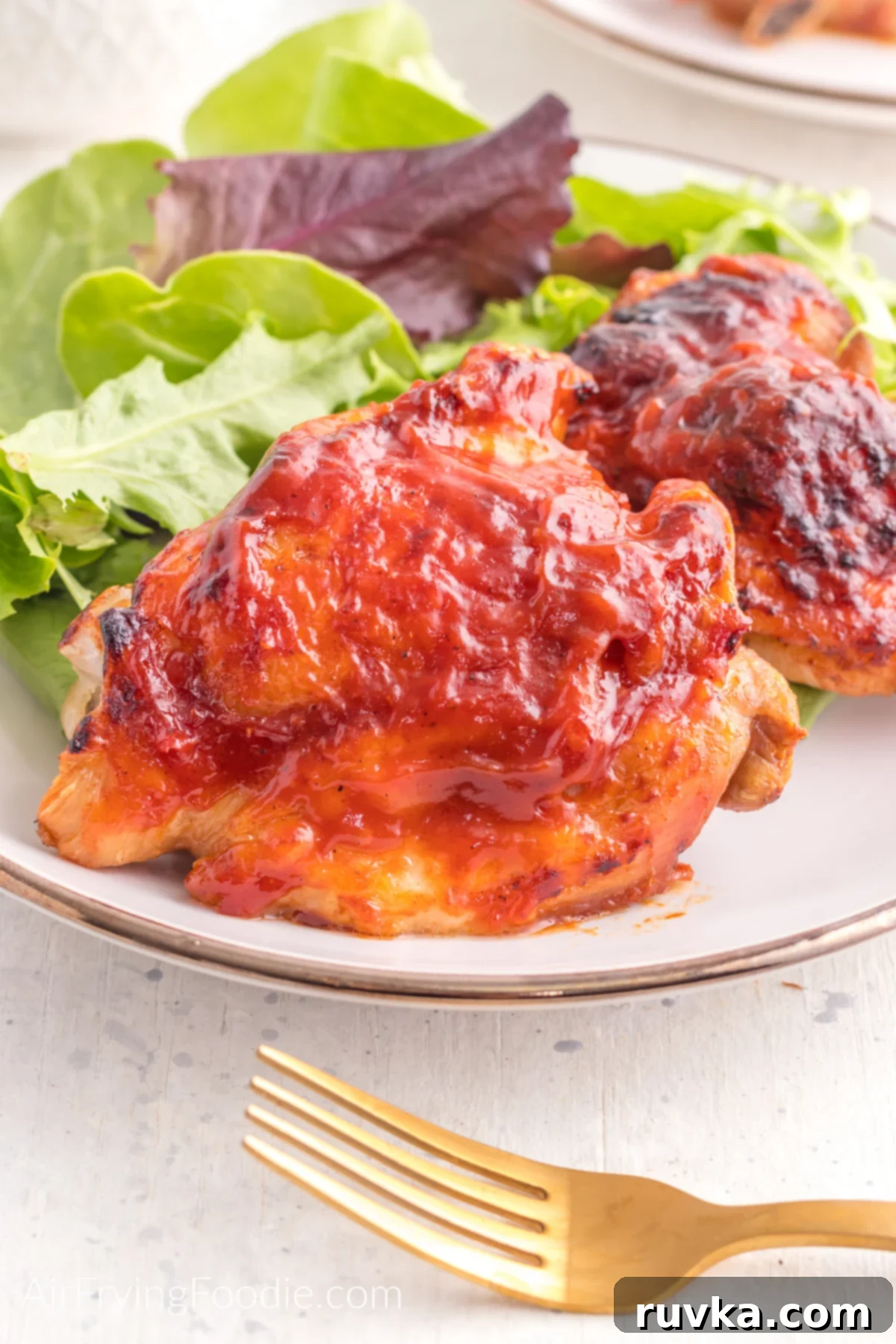 Perfect Air Fryer BBQ Chicken Thighs 2 BBQ chicken made in the air fryer on a plate with a side of salad.