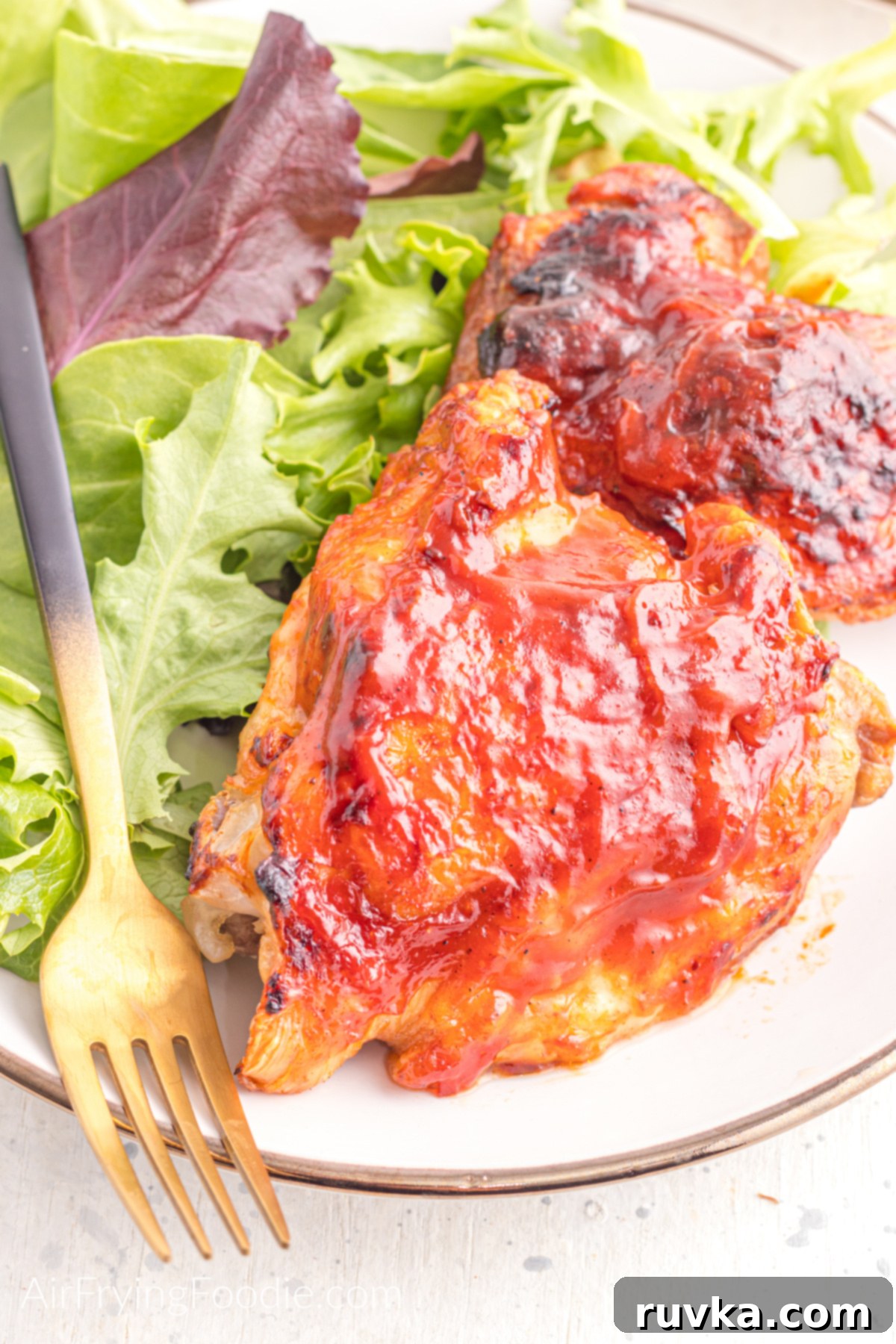 Perfect Air Fryer BBQ Chicken Thighs 3 Close up of BBQ chicken thighs made in the air fryer, served on a plate with a side salad.