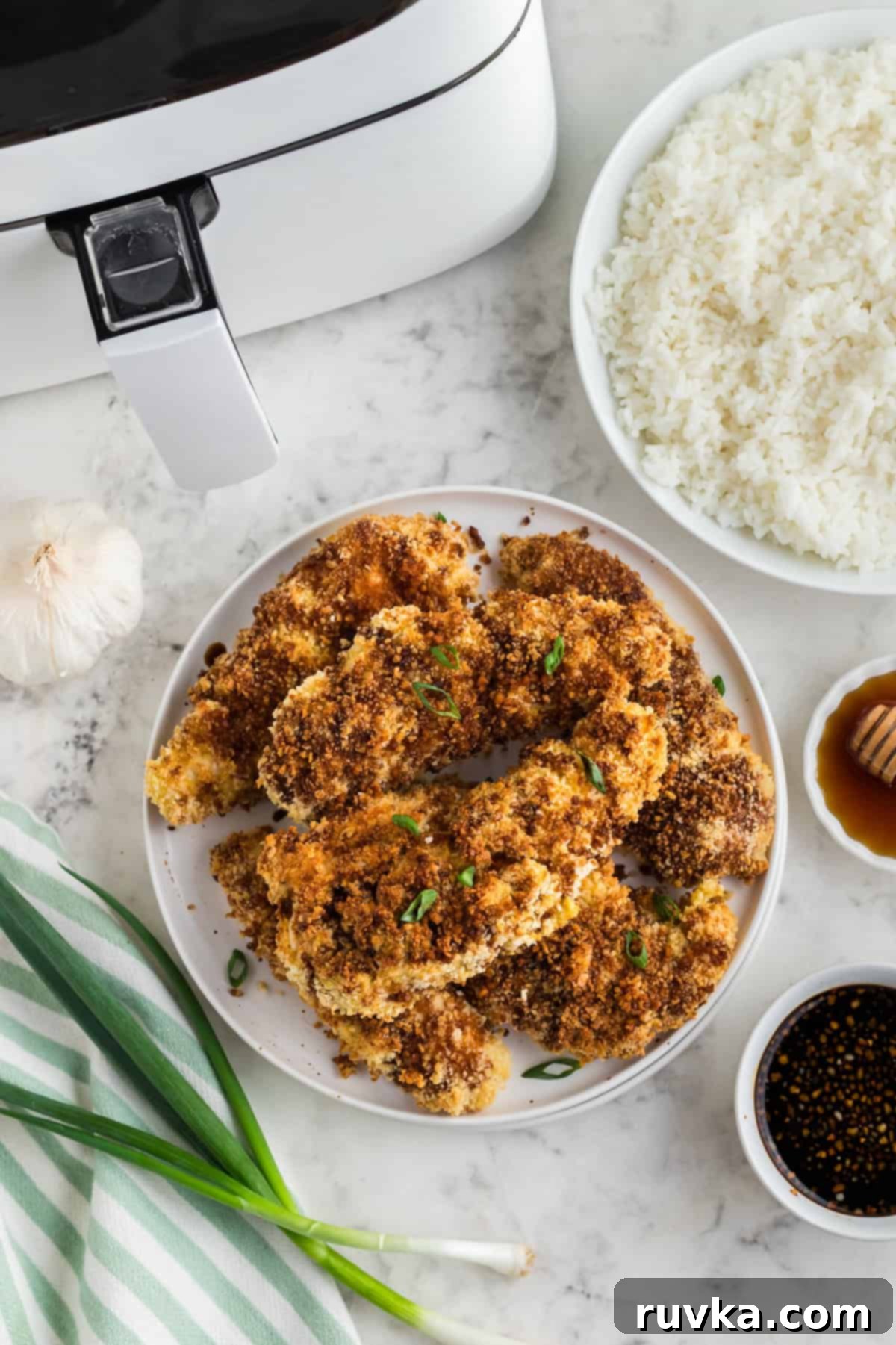 Crispy Air Fried Honey Garlic Chicken Strips 2 Crispy Air Fryer Honey Garlic Chicken Tenders served on a white plate with a fresh garnish.