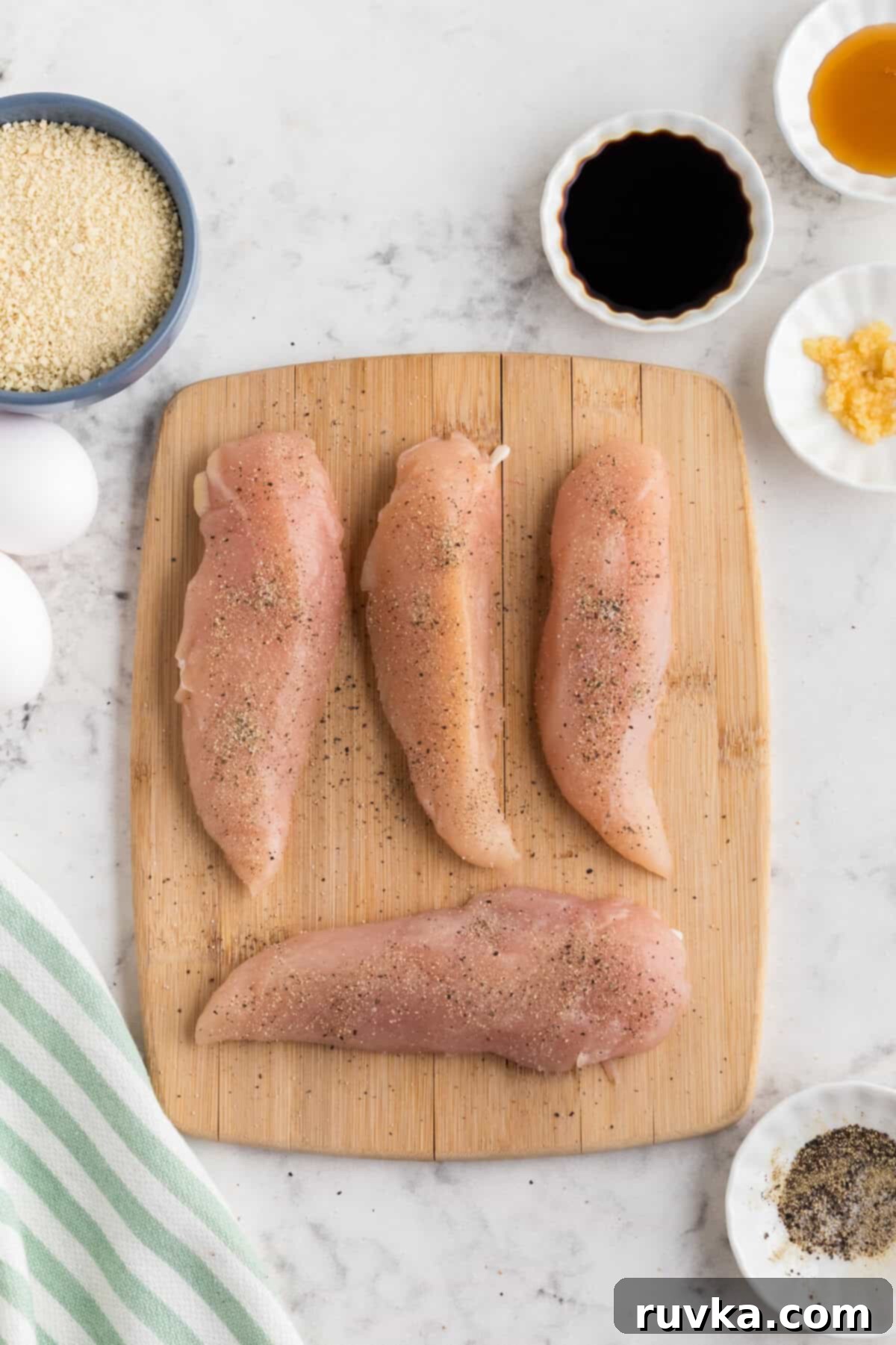 Crispy Air Fried Honey Garlic Chicken Strips 5 Chicken tenders being seasoned with salt and pepper on a cutting board.