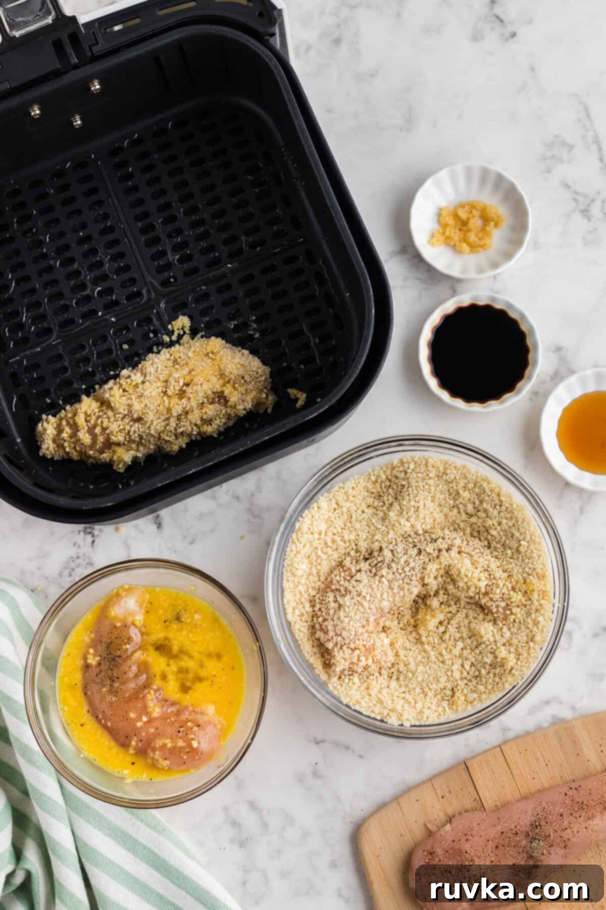 Crispy Air Fried Honey Garlic Chicken Strips 6 Chicken tender being dipped into a bowl of whisked eggs, then into a bowl of Panko breadcrumbs.