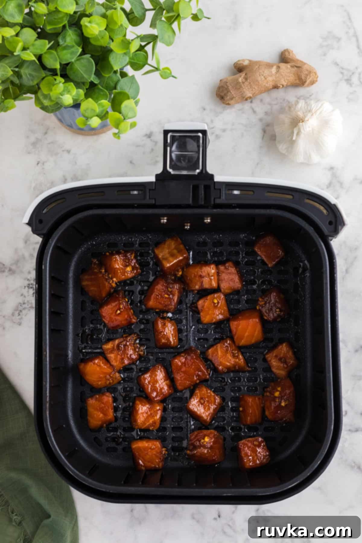 Step 4: Marinated salmon bites carefully arranged in a single layer in the Air Fryer basket, which is lined with parchment paper, ensuring ample space between pieces.